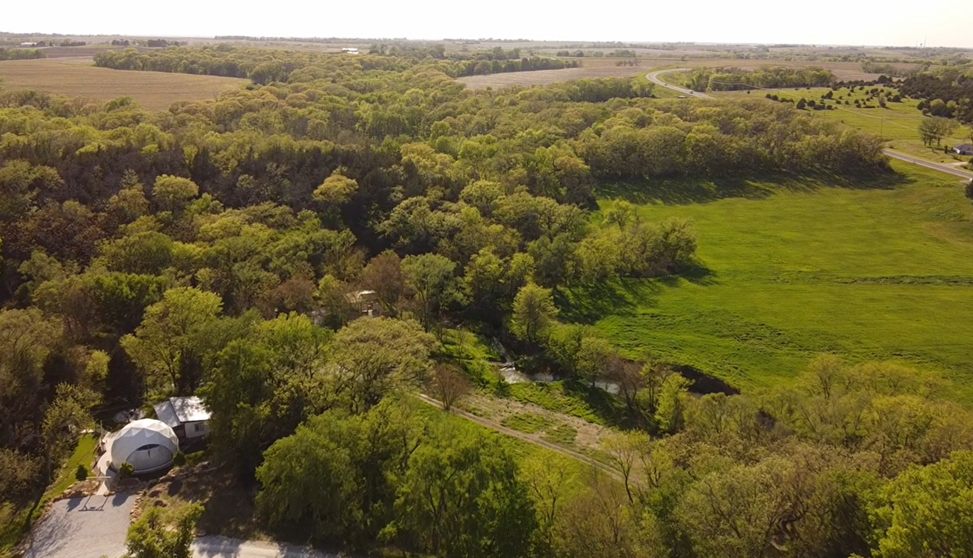 Aerial of the glampgrounds — the creek winding through the wooded property past the dome